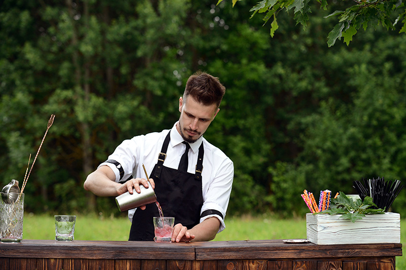 Residential event staff bartender prepares cocktails at an outdoor gathering.