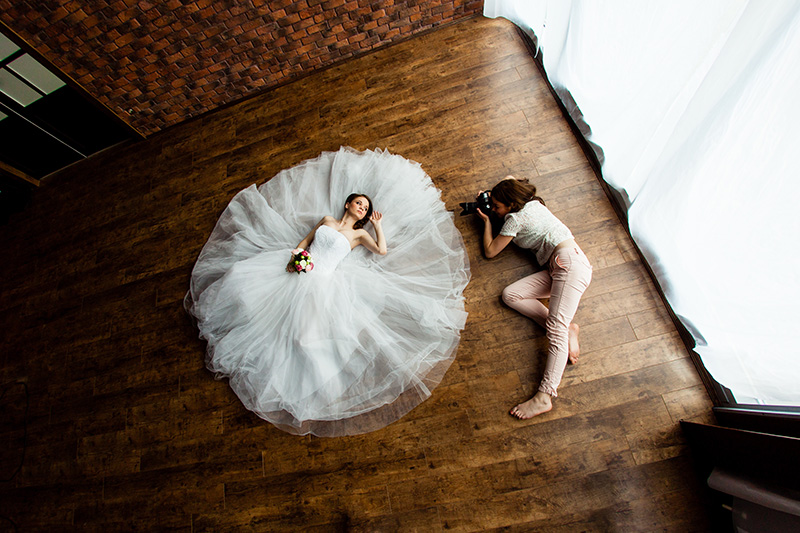 A wedding bride poses for a wedding photographer at an event rental venue on the floor in a flowing white wedding dress